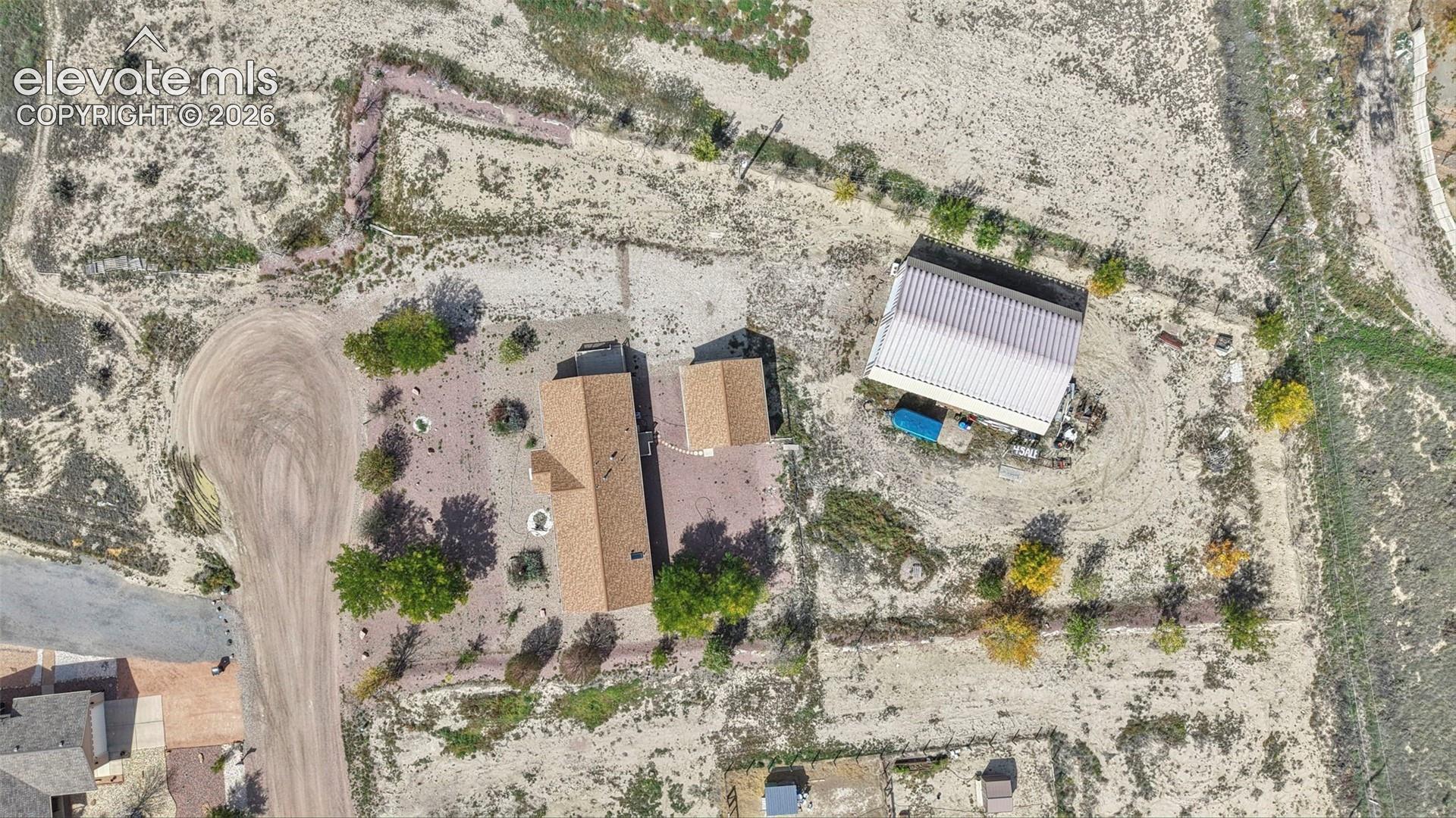 Aerial view of a sprawling property featuring a primary residence with a shingled roof, a secondary detached structure with a metal roof, and established trees throughout the grounds