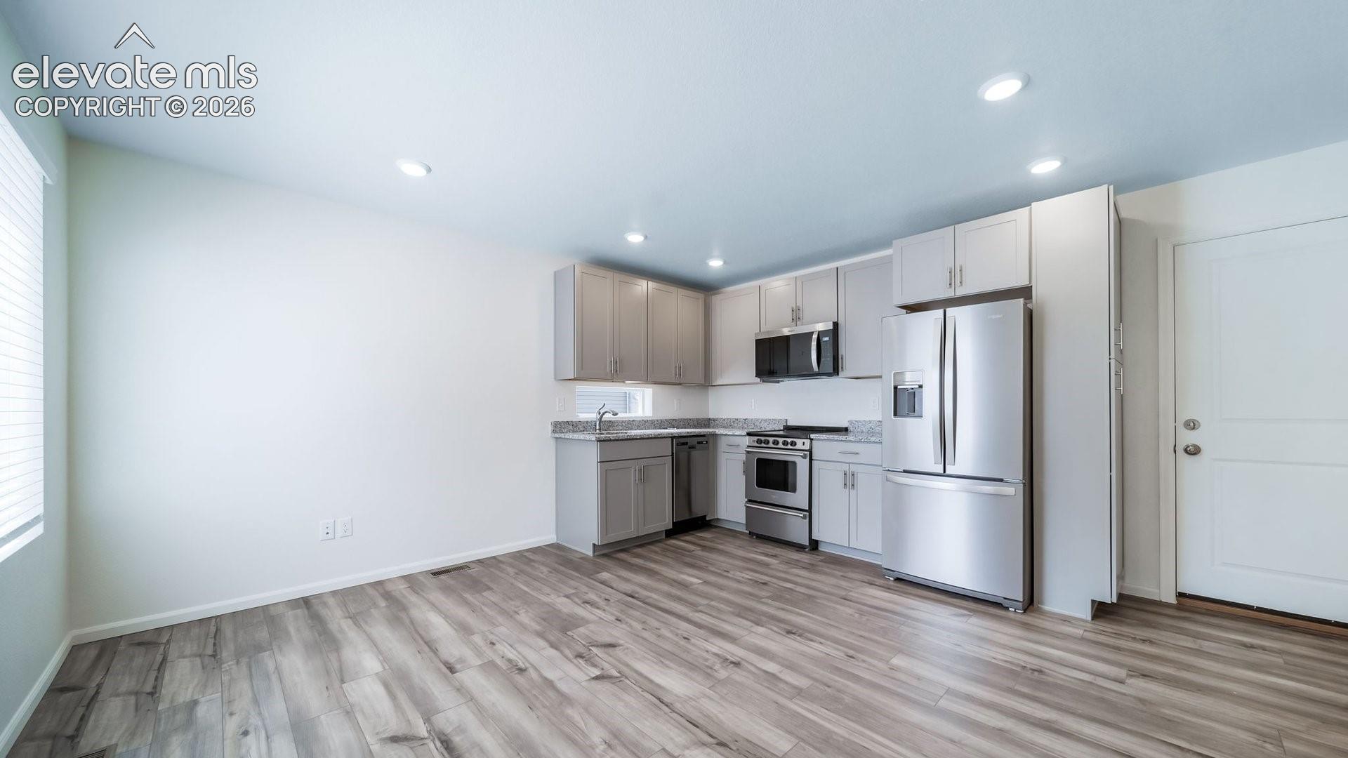 Kitchen featuring shaker-style cabinetry, stone-finish countertops, stainless steel appliances, and wood-finish flooring
*photos of a model home*