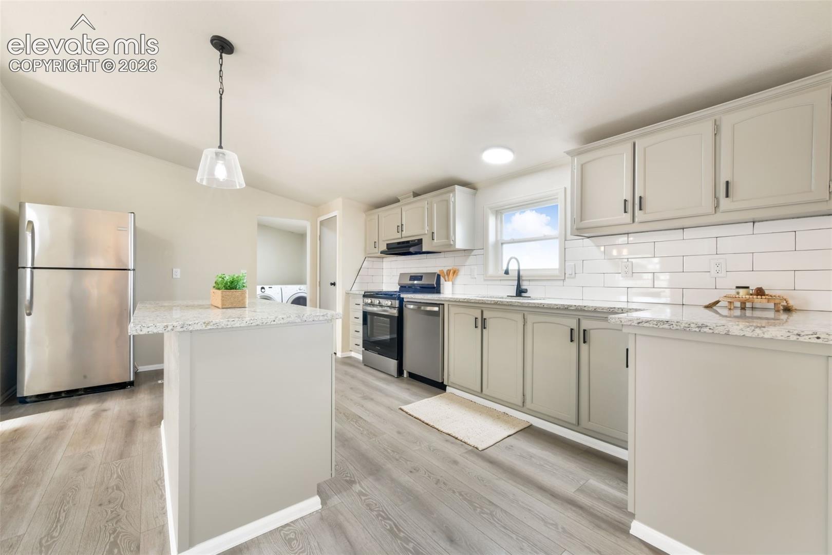 Kitchen featuring stainless steel appliances, light-toned cabinetry, granite-finish countertops, subway tile backsplash, and wood-finish flooring