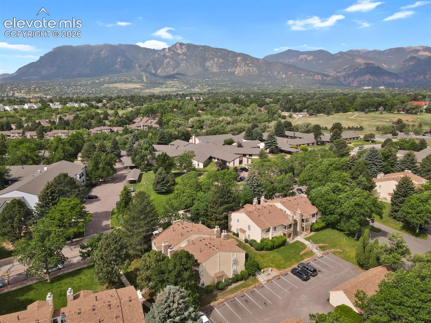 Aerial perspective featuring mature tree landscaping, designated surface parking, and a mountain backdrop.  Photo taken in the summer