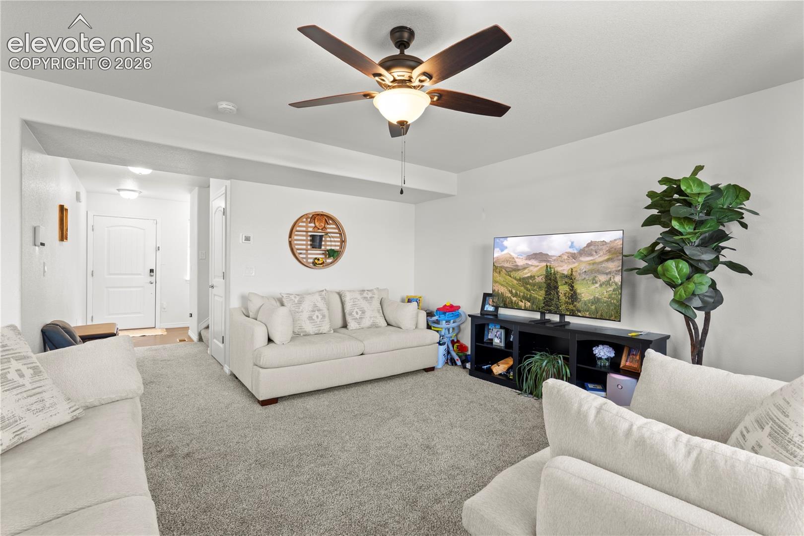 Living area featuring neutral carpeting, a ceiling fan with integrated lighting, and a six-panel interior door