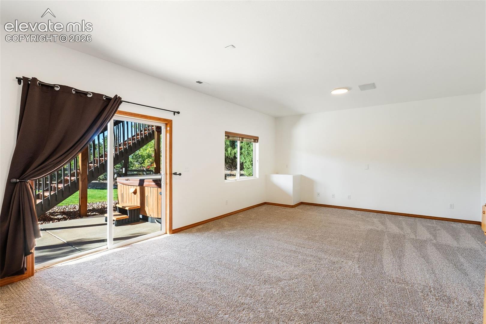 Neutral-toned carpeting, sliding glass doors, wooden exterior staircase, and a concrete patio