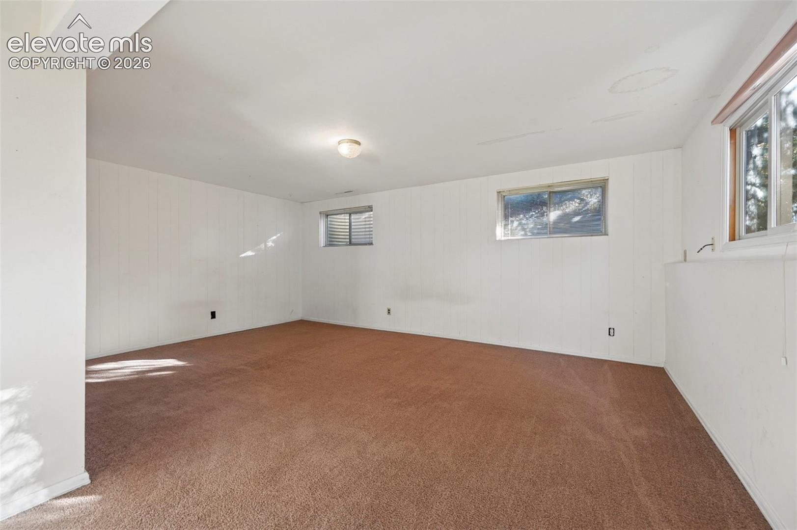 Expansive room featuring carpet flooring, white paneled walls, and multiple windows