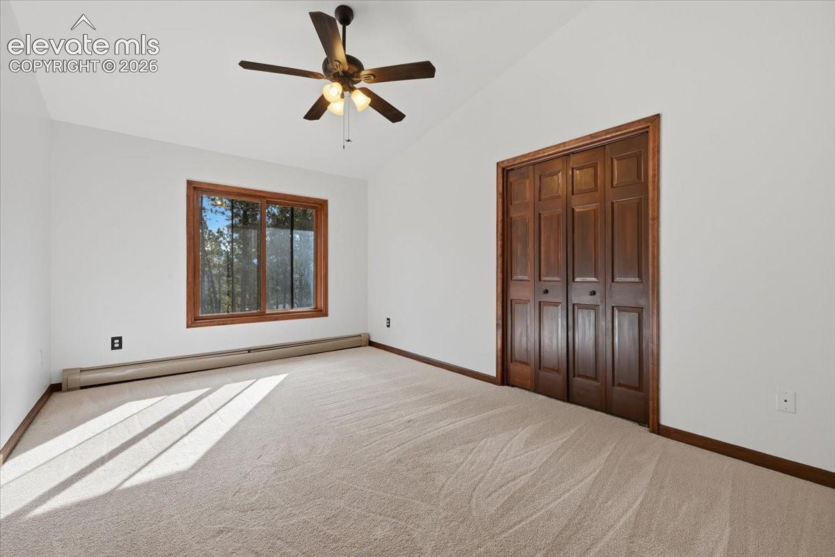 Vaulted ceiling with an attached ceiling fan and light fixture, featuring a window with wood trim, wall-to-wall carpeting, and wood bifold closet doors