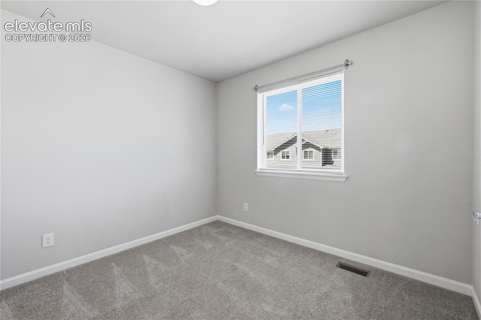 Bright room featuring a double-paned window with horizontal blinds, neutral gray carpeting, and light gray wall paint