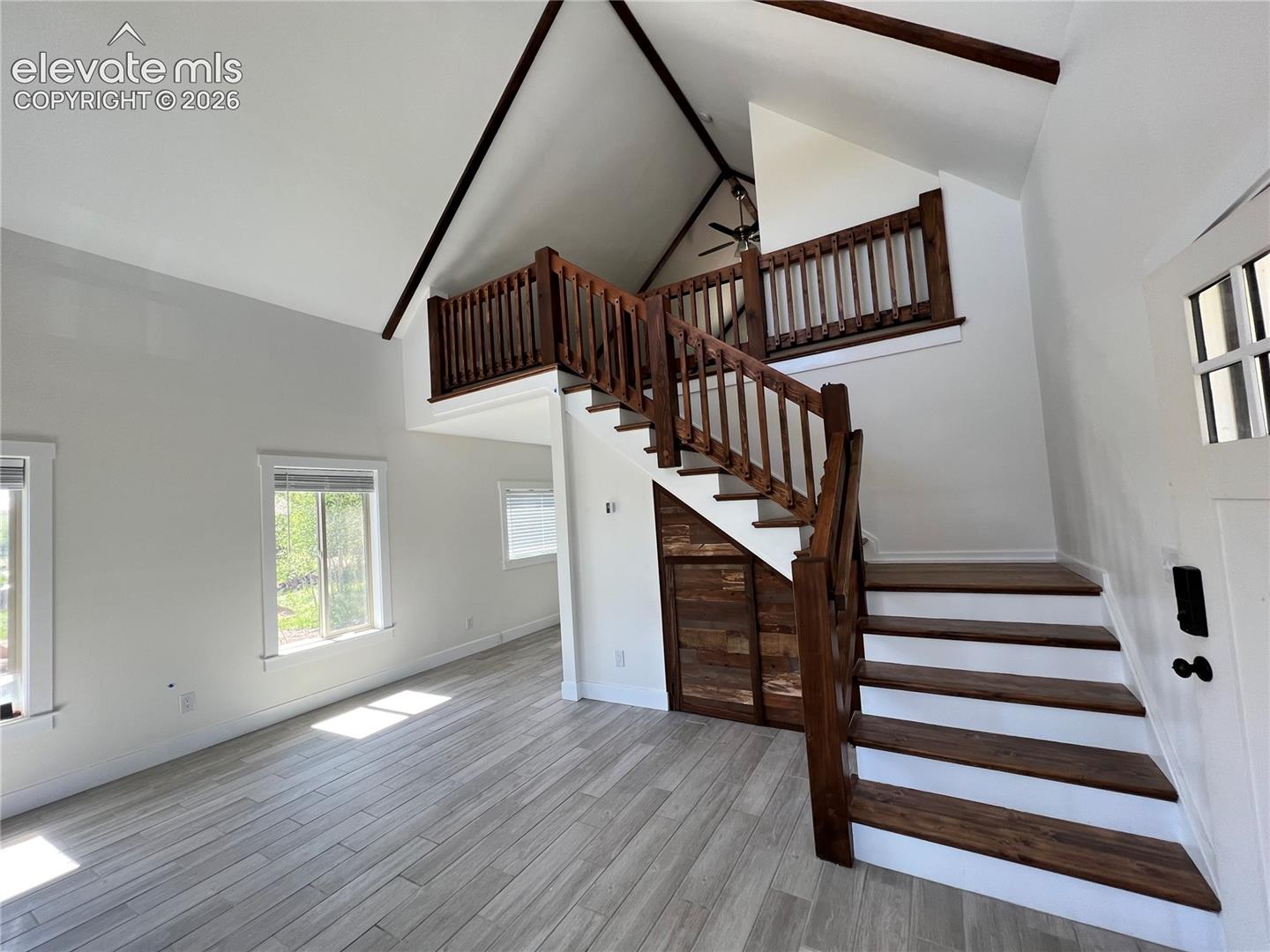 Vaulted ceilings with exposed beams, wood-finish flooring, staircase with wood risers and balusters, and a loft area with wood railing