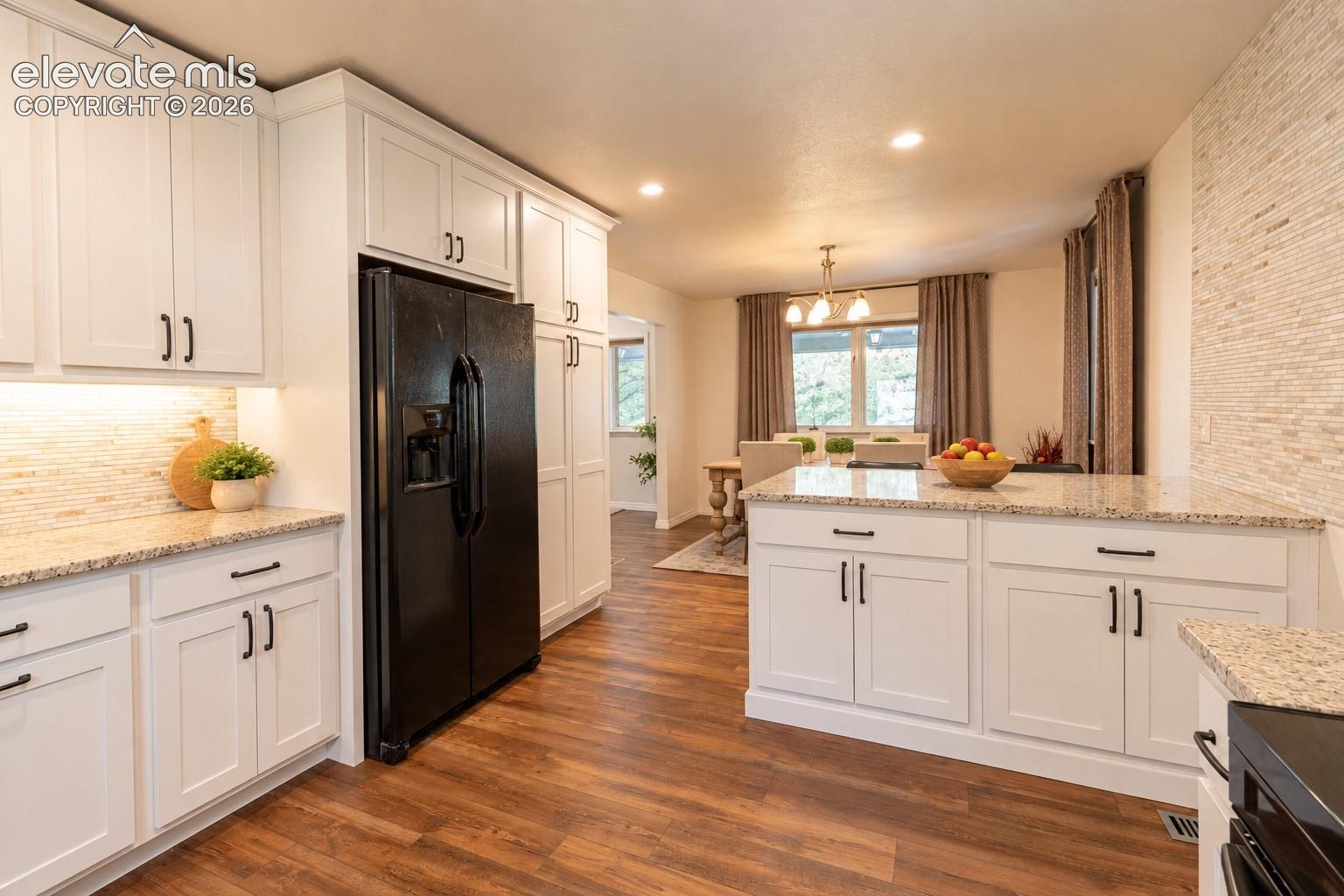 Kitchen featuring white cabinetry, granite countertops, wood-finish flooring, a tile backsplash, and a black side-by-side refrigerator