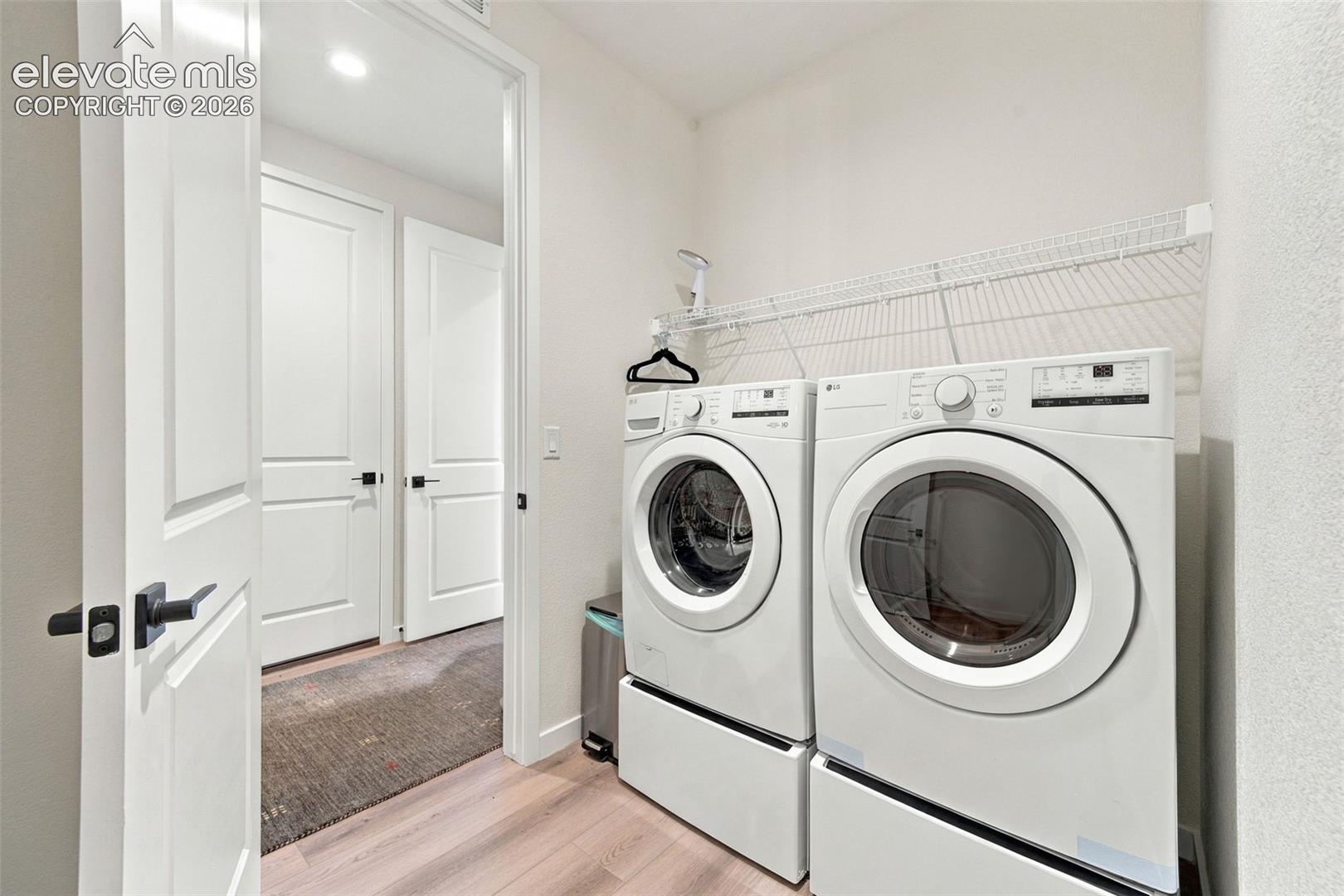 Laundry area featuring wood-finish flooring, two-panel interior doors with matte black hardware, and built-in wire shelving