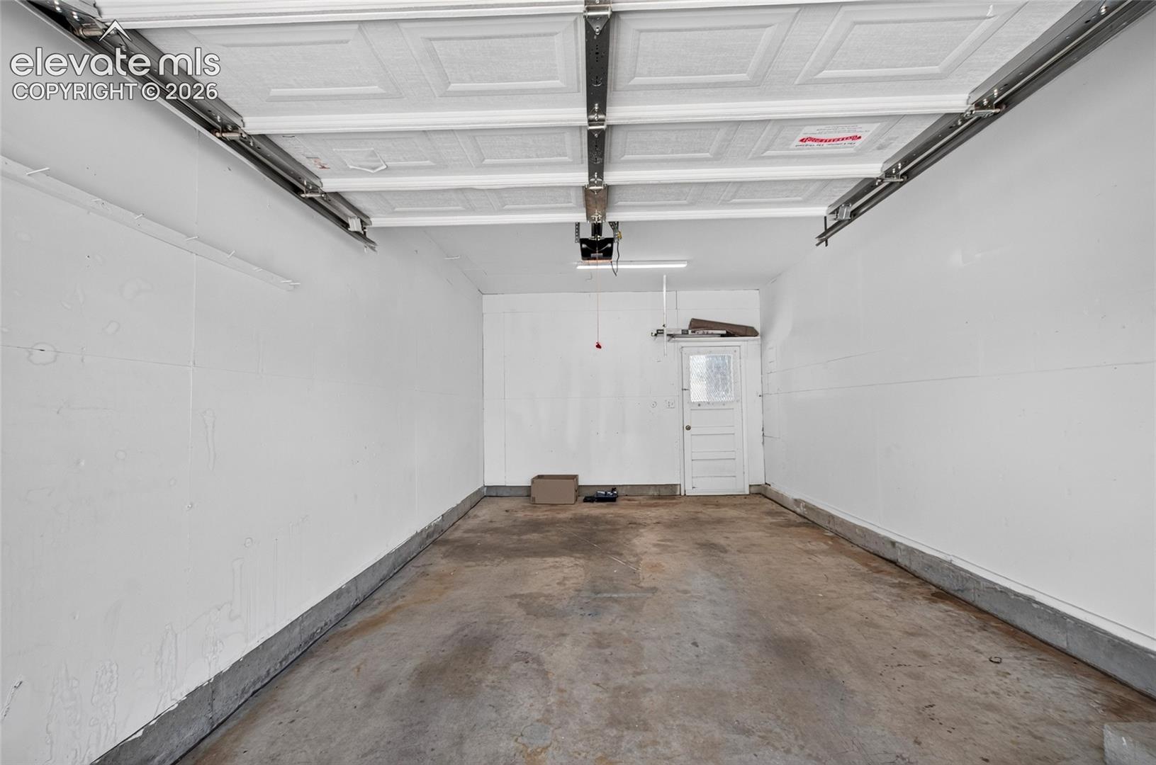 Garage interior with white painted walls, concrete flooring, and an overhead garage door mechanism
