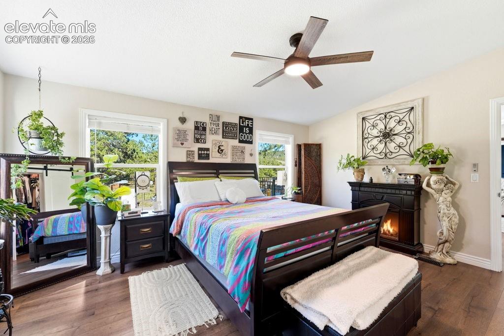 Wood-finish flooring, ceiling fan with integrated lighting, multiple windows, and a built-in fireplace feature