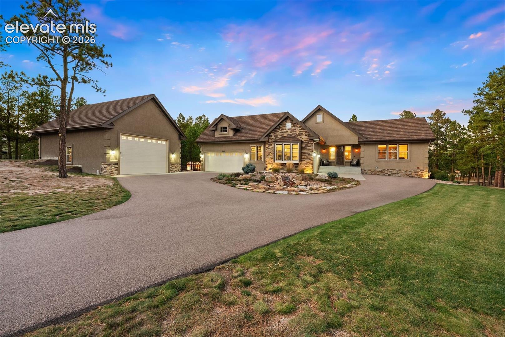 Single-story exterior featuring stone veneer accents, a paved circular driveway, a multi-car garage, and a central rock garden landscape