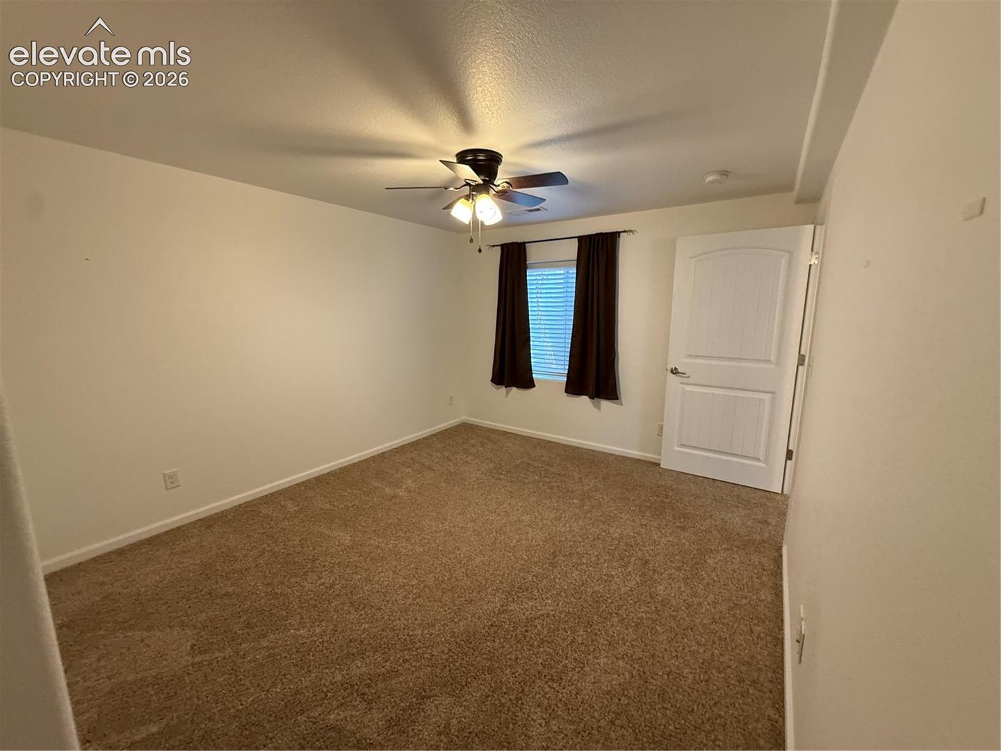 Neutral-toned wall-to-wall carpeting, ceiling fan with integrated light fixture, multi-panel interior door, and window with blinds