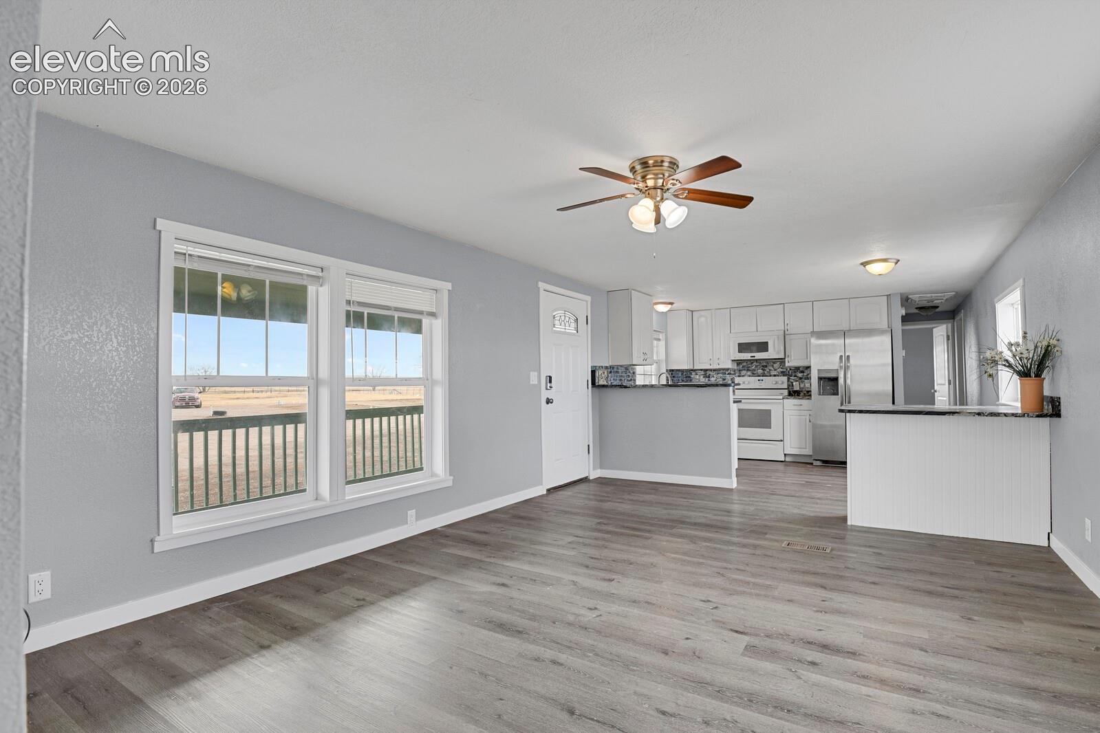 Open-concept living space featuring wood-finish flooring, a ceiling fan, and a kitchen with white cabinetry, stainless steel appliances, and granite-style countertops