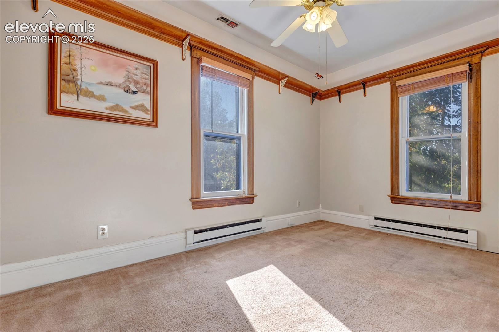 High ceilings featuring decorative wood picture rail molding, two windows with wood casing, and a central ceiling fan