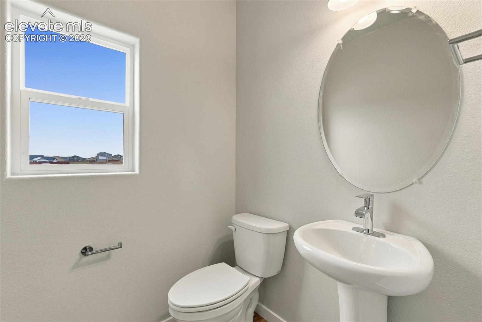 Oval wall-mounted mirror, pedestal sink with chrome faucet, and single-hung window with a neutral interior finish