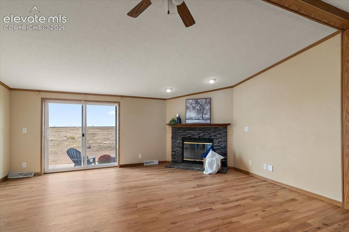 Living area with wood-finish flooring, a stone-clad fireplace with a wood mantle, and recessed lighting