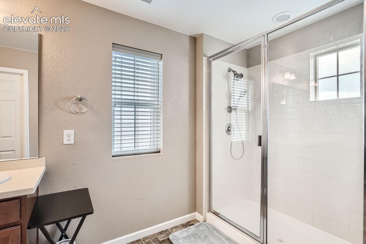Bathroom featuring a walk-in shower with a glass enclosure, tile surround, and chrome hardware, complemented by a vanity with a solid-surface countertop and neutral-toned wall finish