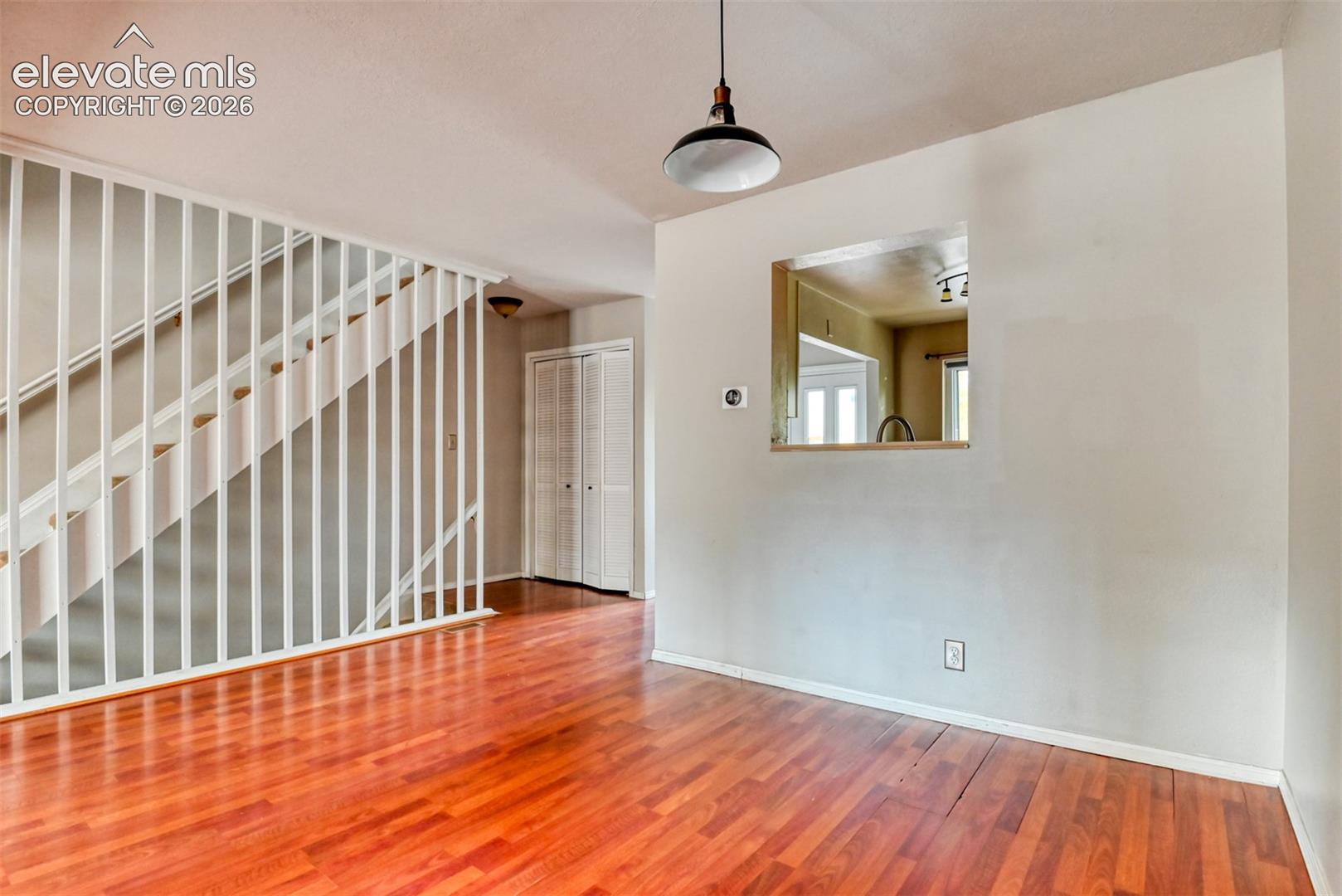 Wood-finish flooring, white spindle stair railing, built-in pass-through window, and a flush-mount ceiling light