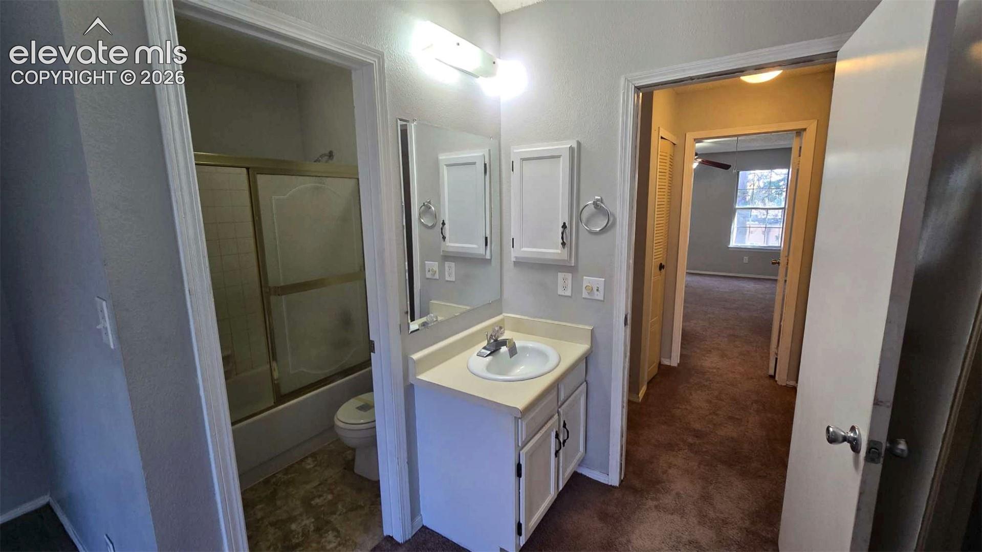Bathroom featuring a vanity with a solid-surface countertop, an integrated sink, and an attached medicine cabinet, complemented by a shower-tub combination with sliding glass doors