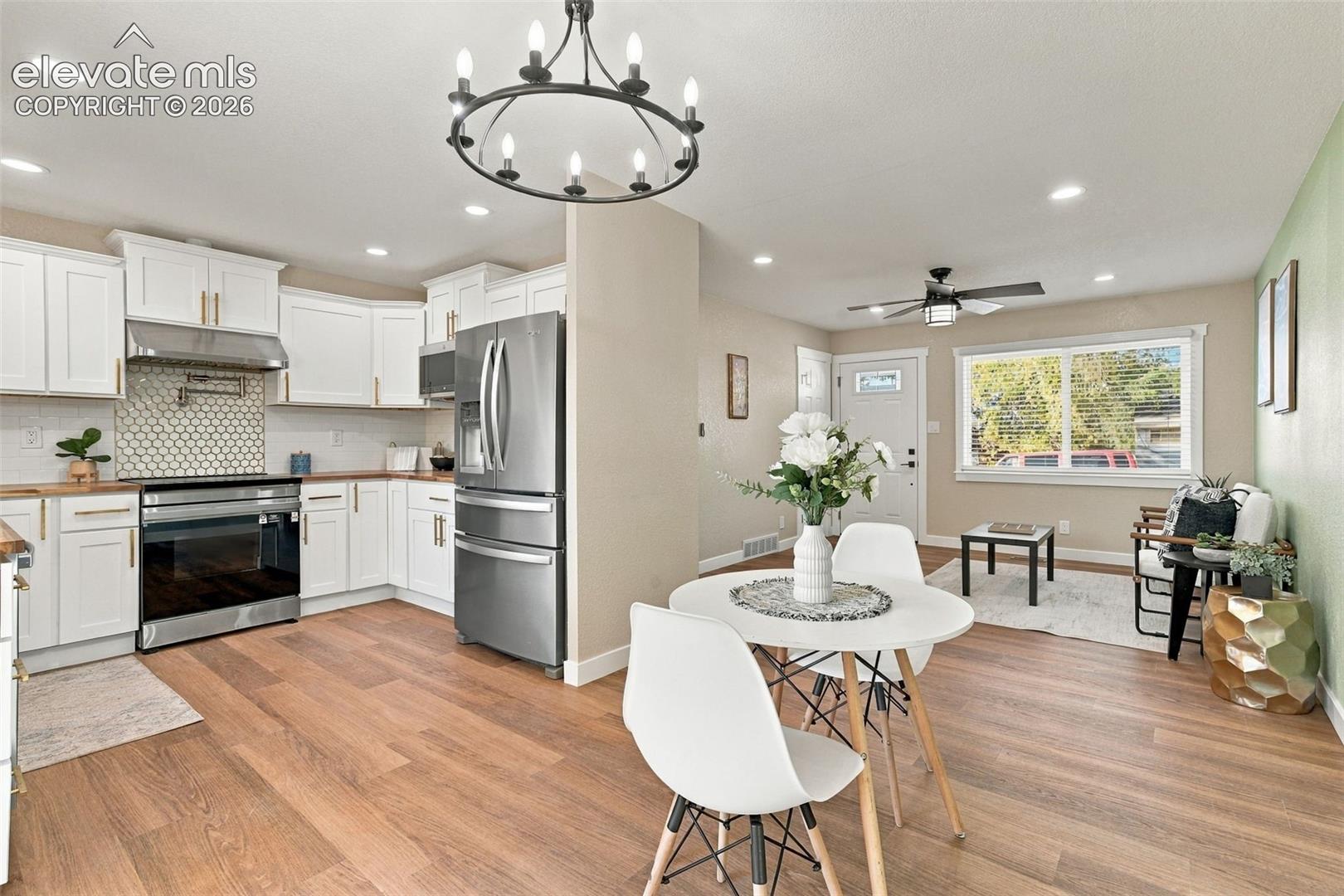 Kitchen featuring white shaker-style cabinetry, stainless steel appliances, a honeycomb-patterned tile backsplash, wood-finish flooring, and a wrought-iron style chandelier