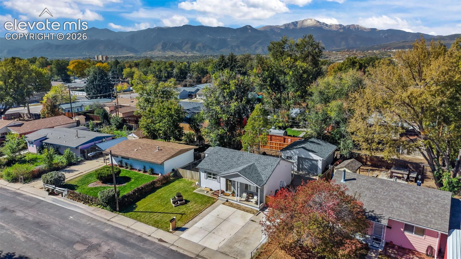 Residential property featuring a concrete driveway, a front-facing covered porch, a detached garage, and a manicured lawn, set against a prominent mountain backdrop