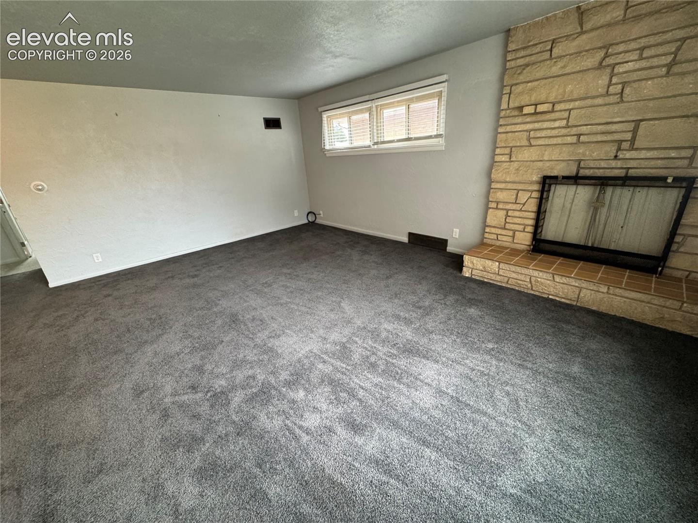Living space featuring neutral carpeting, a floor-to-ceiling stone fireplace, and a tiered stone hearth