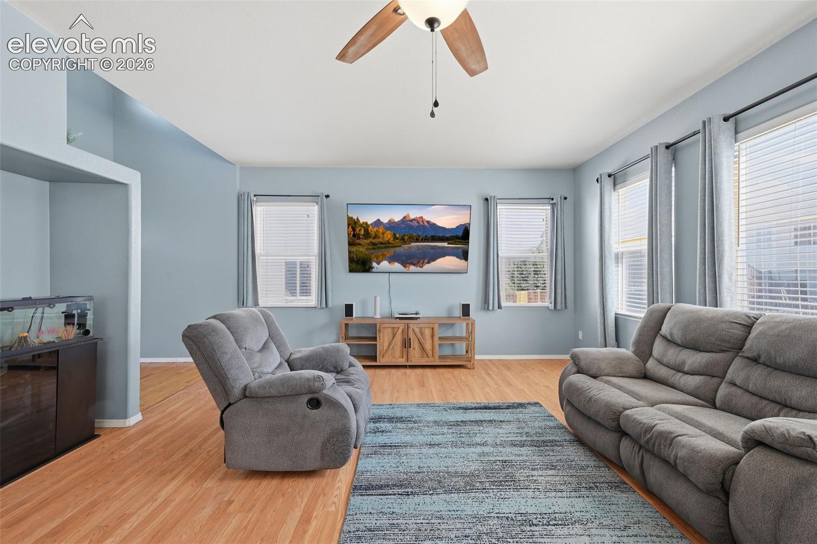 Open-concept living area featuring wood-finish flooring, multiple windows, and a ceiling fan