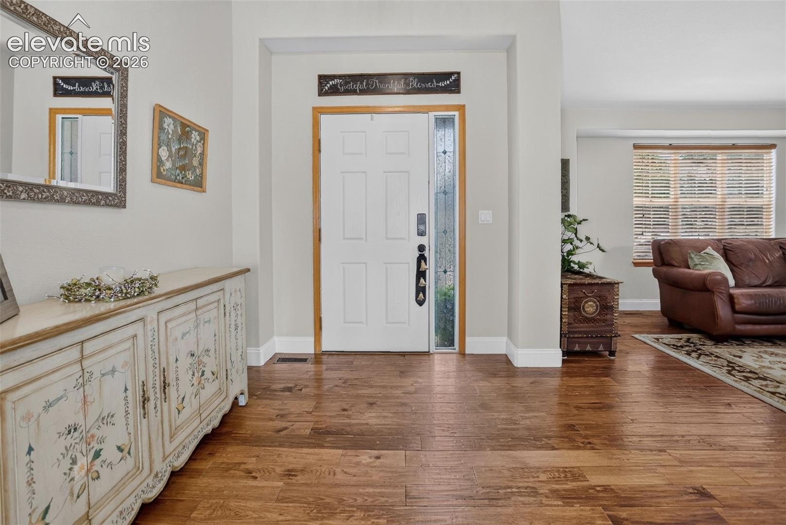Entryway with wood-finish flooring, a white paneled entry door, and a sidelight with decorative glass