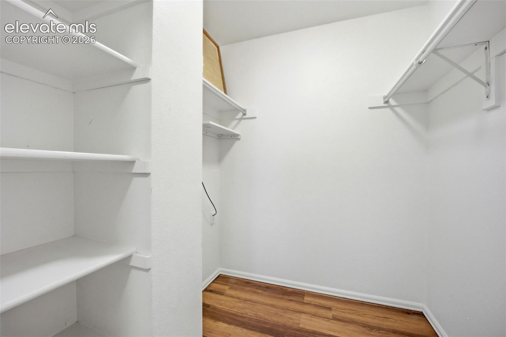 Storage space featuring wood-finish flooring, multi-level shelving, and mounted garment rods