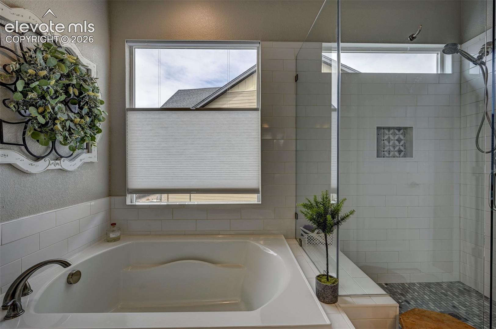 Soaking tub with brushed nickel fixtures, subway tile surround, separate glass-enclosed shower with tiled bench, and decorative shower niche