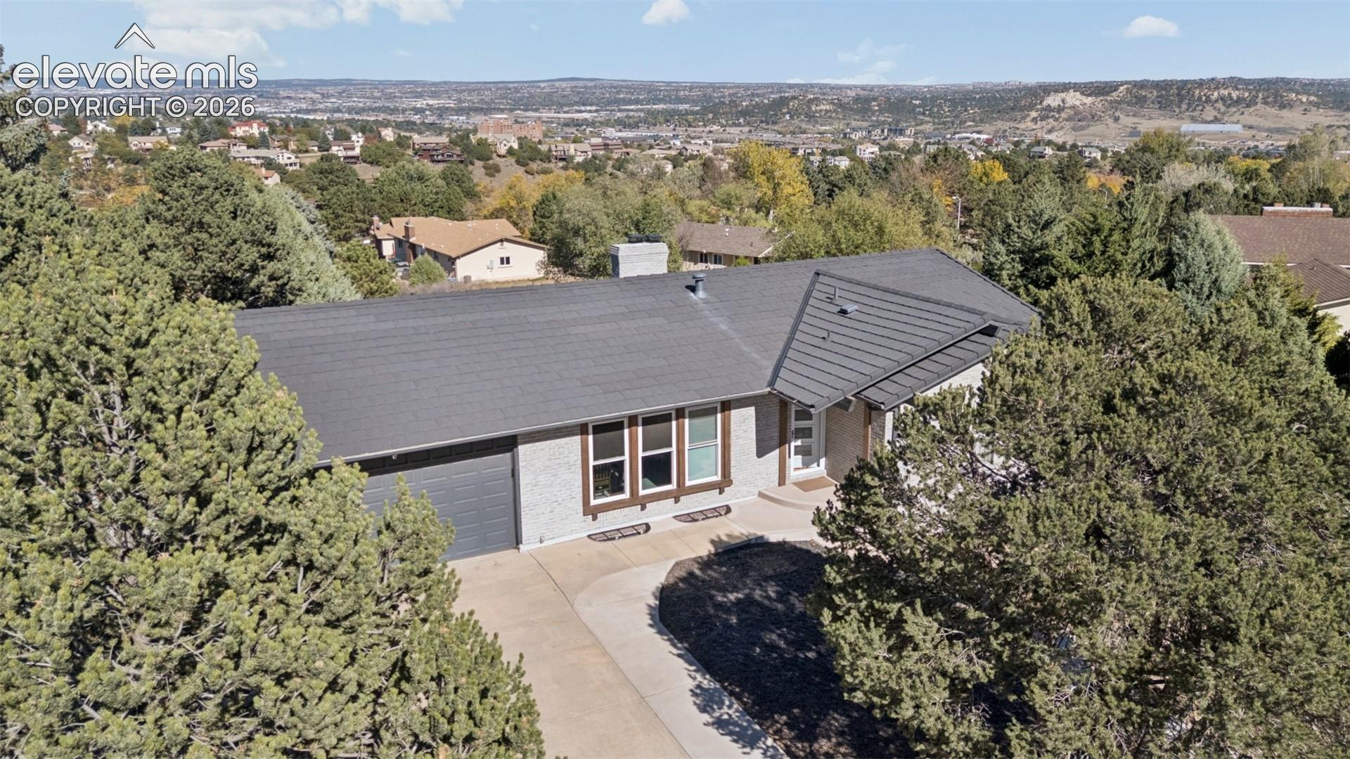 Single-story residence featuring a painted brick exterior, a multi-paneled gable roof, attached garage, concrete driveway, and mature landscaping