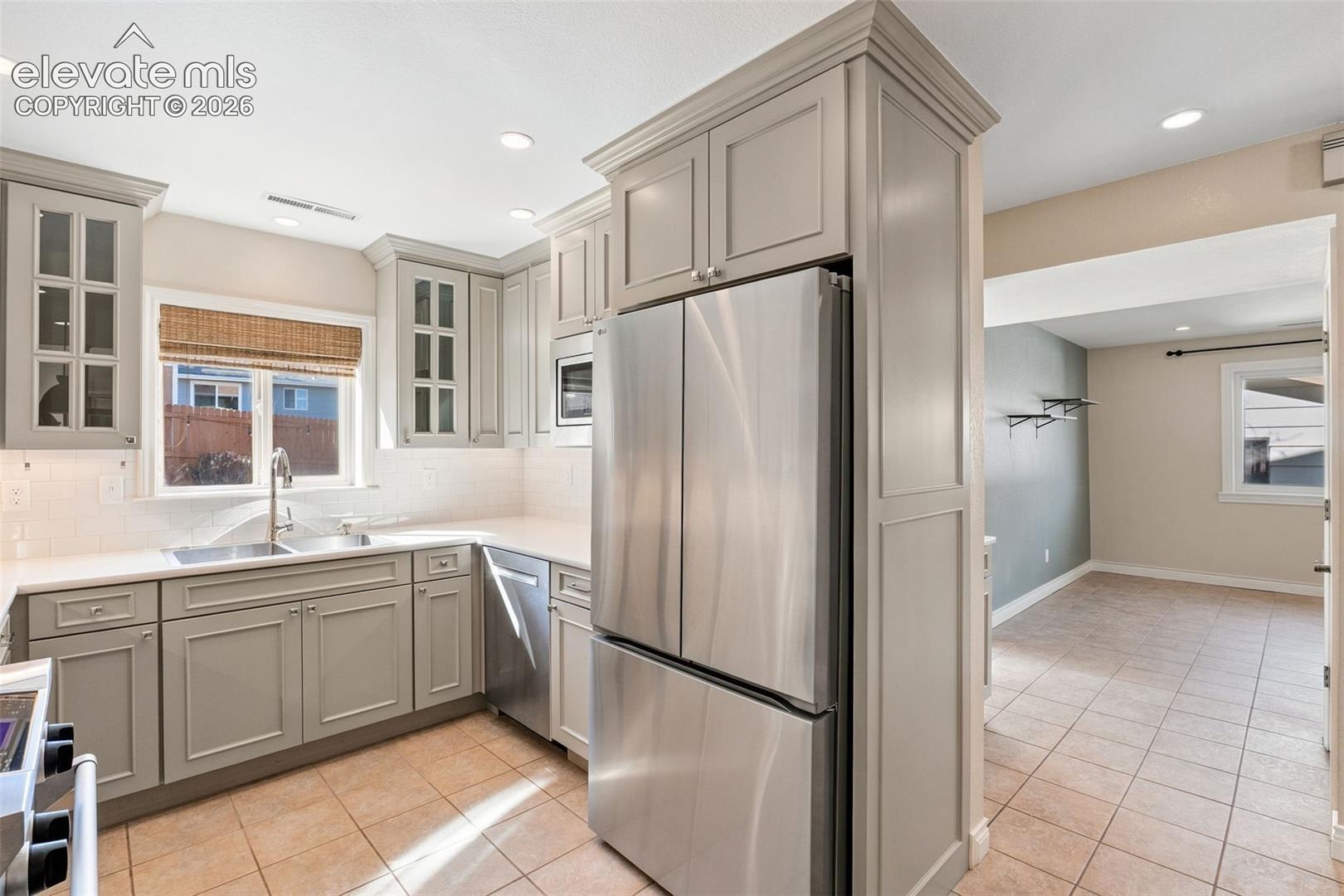 Kitchen featuring custom shaker-style cabinetry with glass-front uppers, stainless steel appliances, solid-surface countertops, and tile flooring