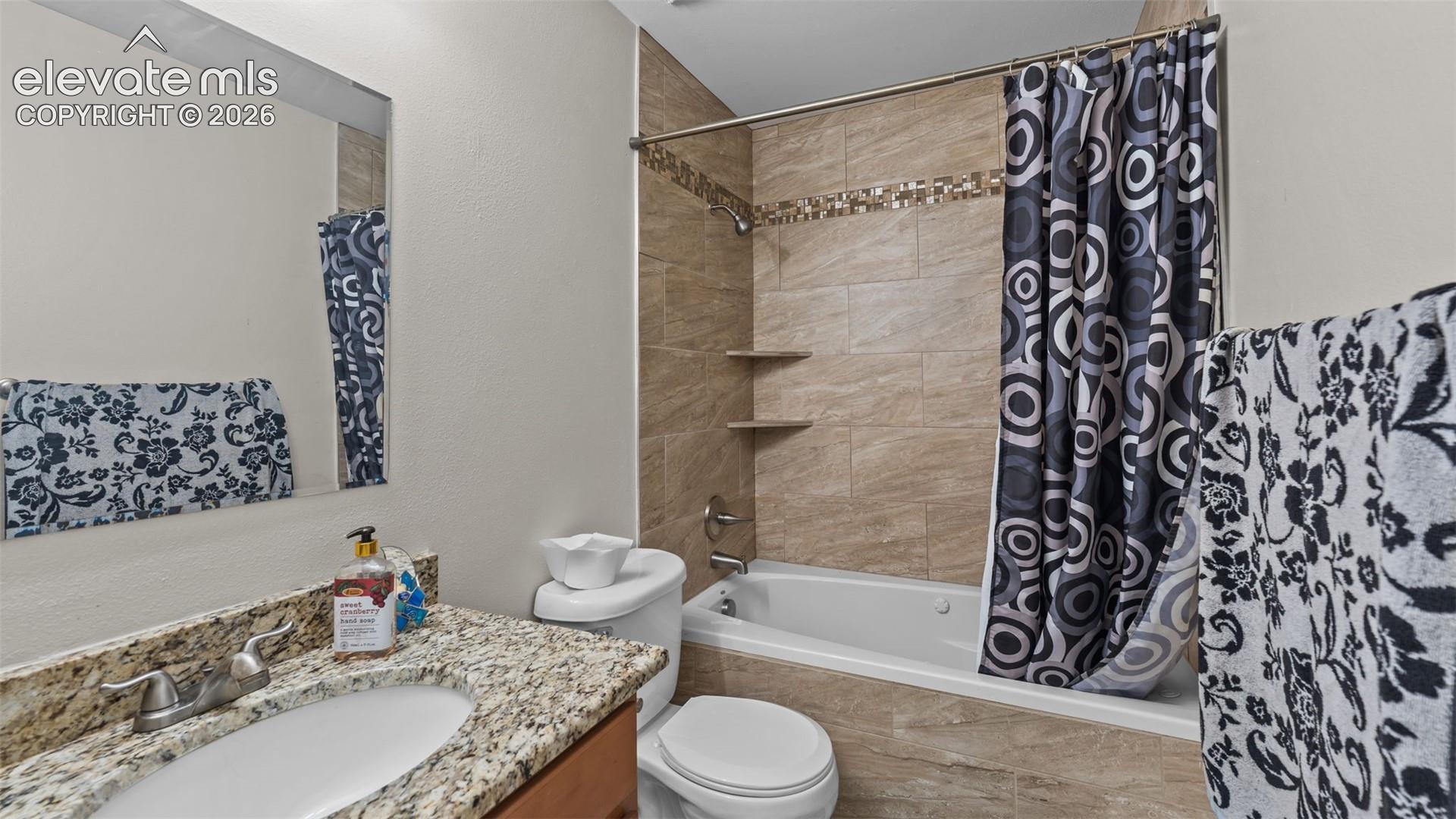 Bathroom featuring a stone-look countertop with an integrated oval sink, a wall-mounted mirror, and a tub-shower combination finished with horizontal wall tile and a mosaic tile accent border