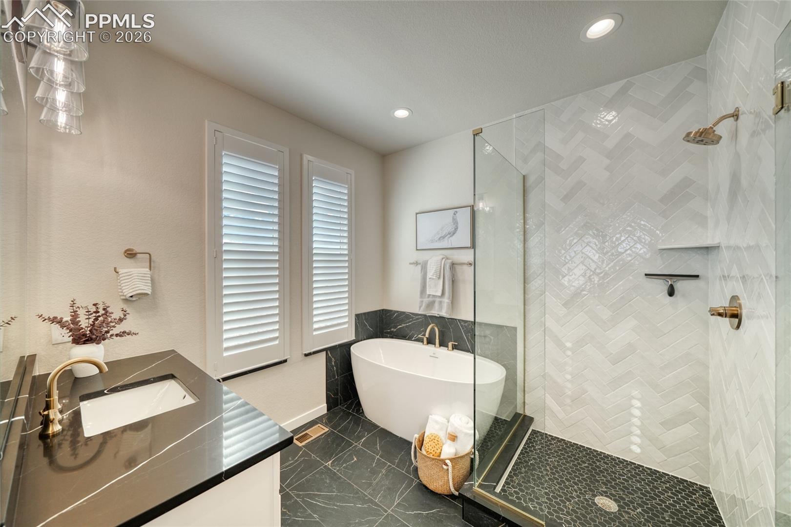 Full bath featuring double vanity, a freestanding tub, a shower stall, recessed lighting, and dark marble finish floors