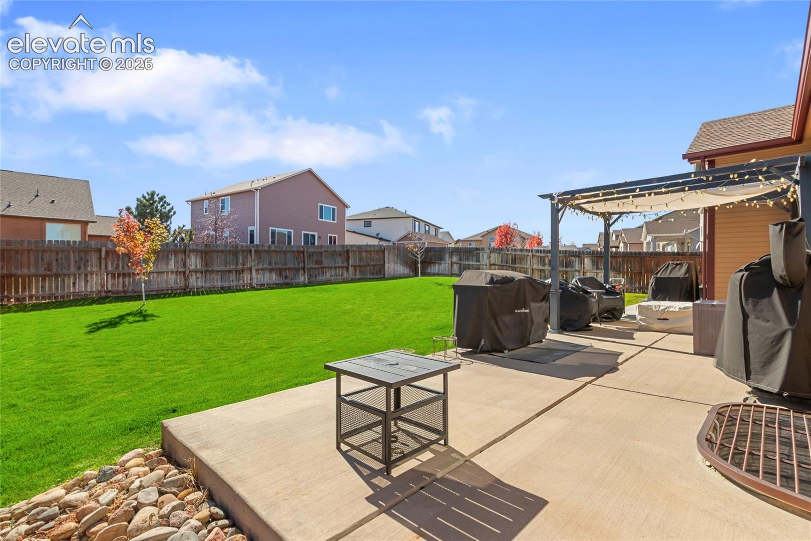 Expansive backyard featuring a manicured lawn, concrete patio, metal pergola, and perimeter wood privacy fencing