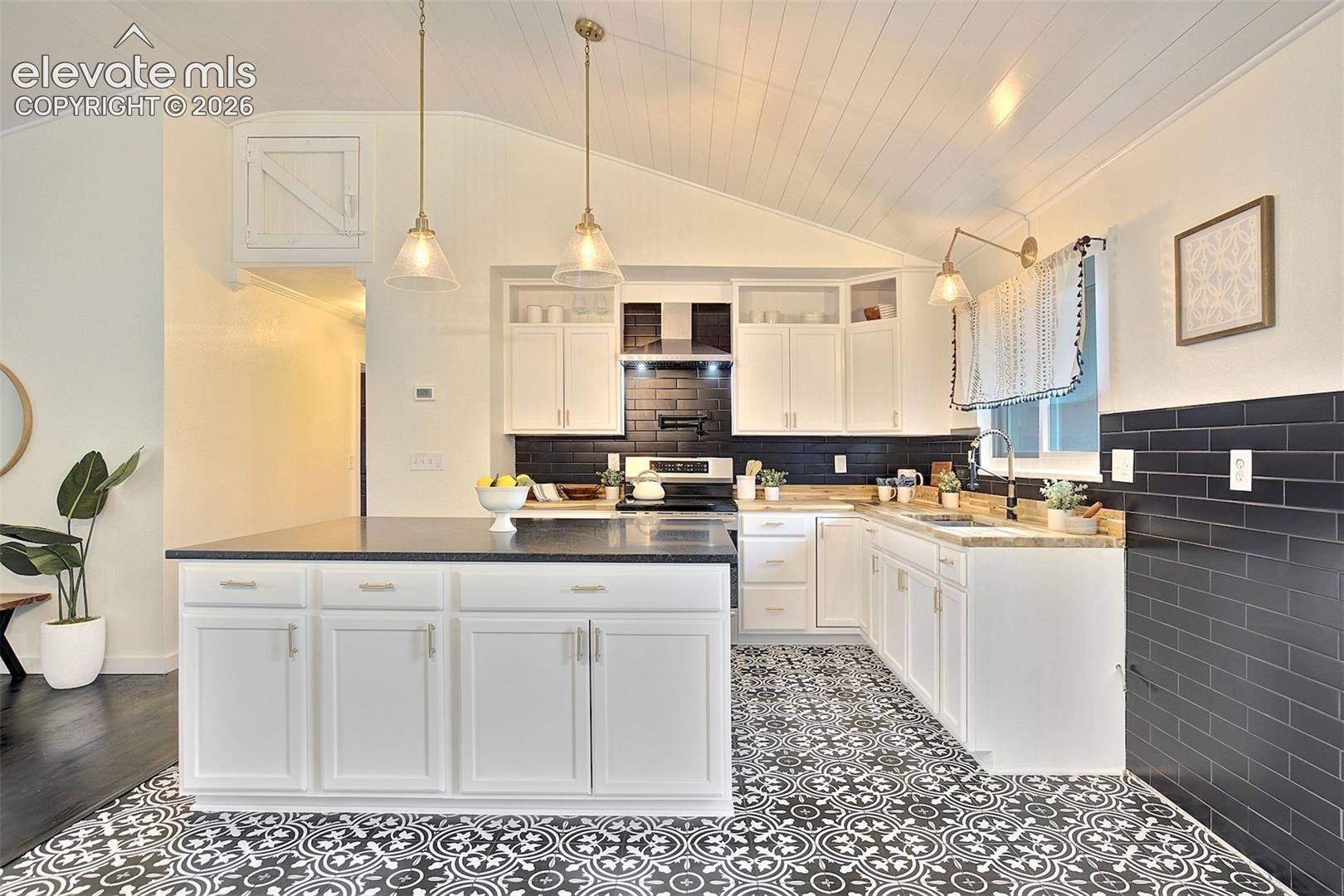 Kitchen featuring a center island with dark countertops, white cabinetry, black subway tile backsplash, patterned tile flooring, and vaulted plank ceiling