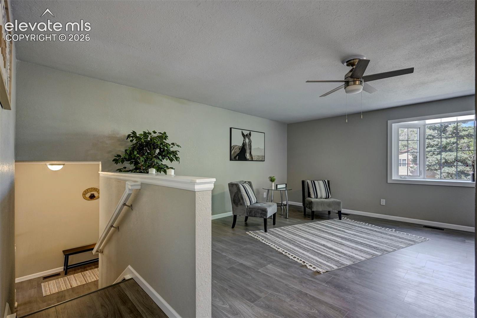 Living area featuring neutral wall paint, wood-finish flooring, a multi-blade ceiling fan, and a wide window with a tiered sill