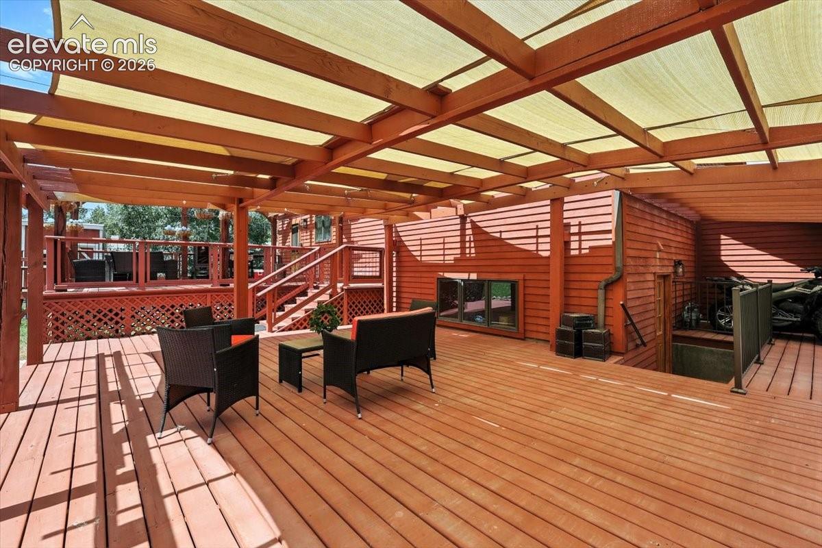 Expansive multi-level wood deck featuring a covered pergola with a tension fabric canopy, wood lattice skirting, and metal railings