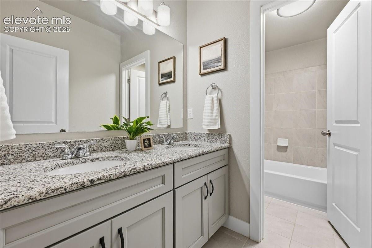 Dual sink vanity with stone-finish countertop, light gray cabinetry, and brushed chrome fixtures