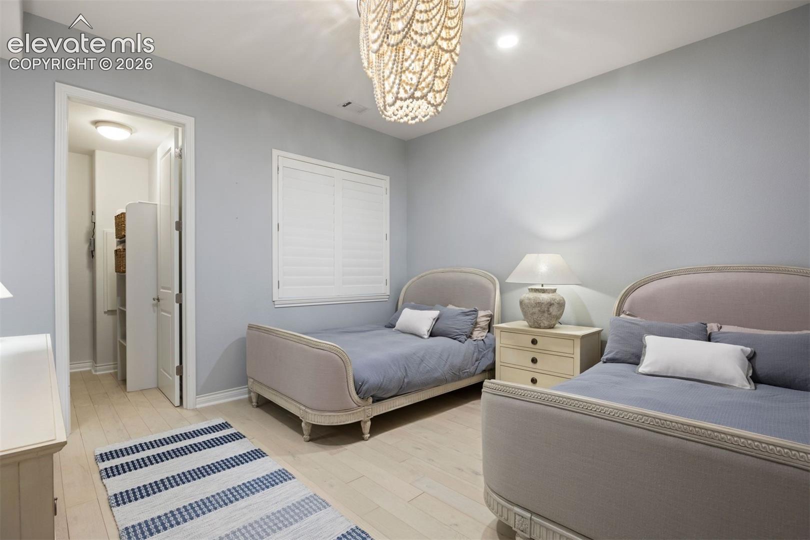 Light-hued wood-finish flooring provides a bright base for this room, featuring a built-in window shutter, a decorative chandelier, and recessed lighting