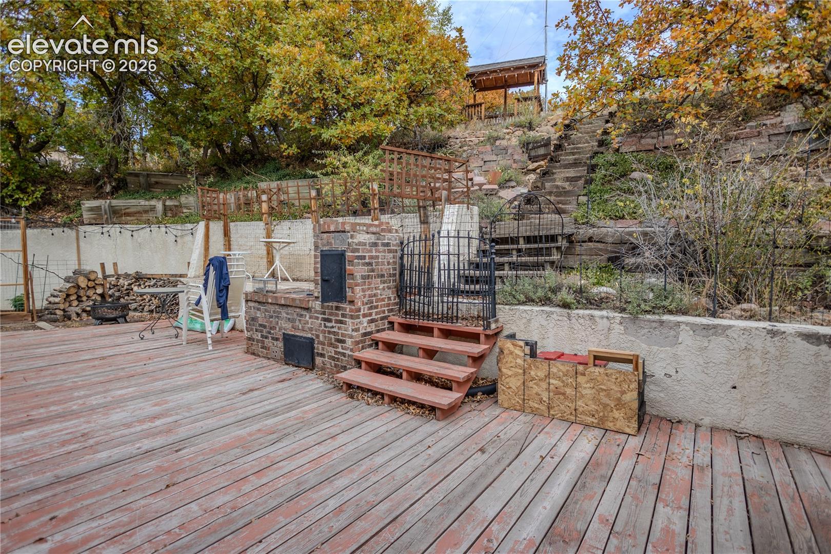 Multi-level deck featuring a built-in brick fireplace, retaining walls, metal security gate, and terraced stone stairs