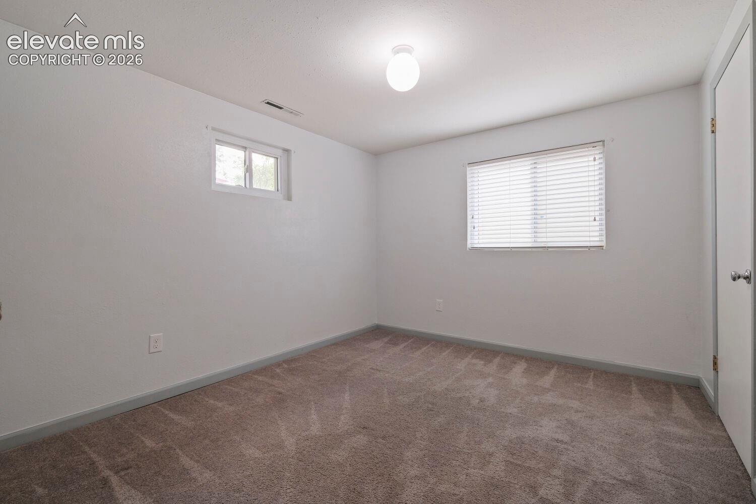 Spacious interior room featuring white painted walls and neutral-toned patterned carpeting