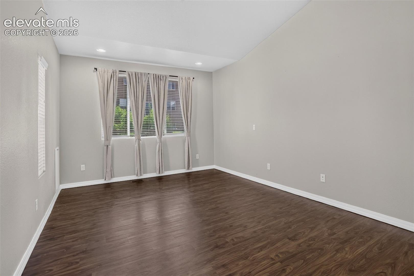 Wood-finish flooring with light gray walls, multiple windows, and a vaulted ceiling with recessed lighting