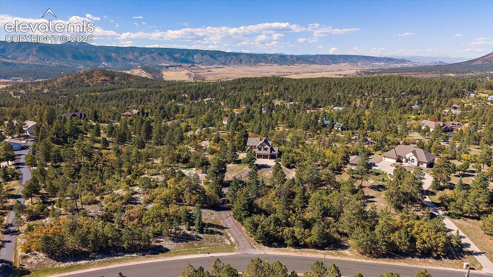 Aerial perspective of a wooded landscape featuring mature pine trees, extensive natural terrain, paved asphalt roads, and mountain backdrops