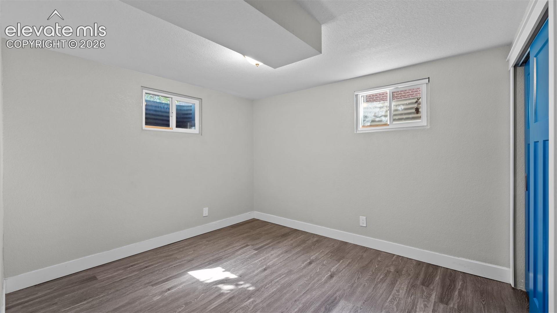 Recessed ceiling light, wood-finish flooring, light gray walls, two windows, and a blue interior door