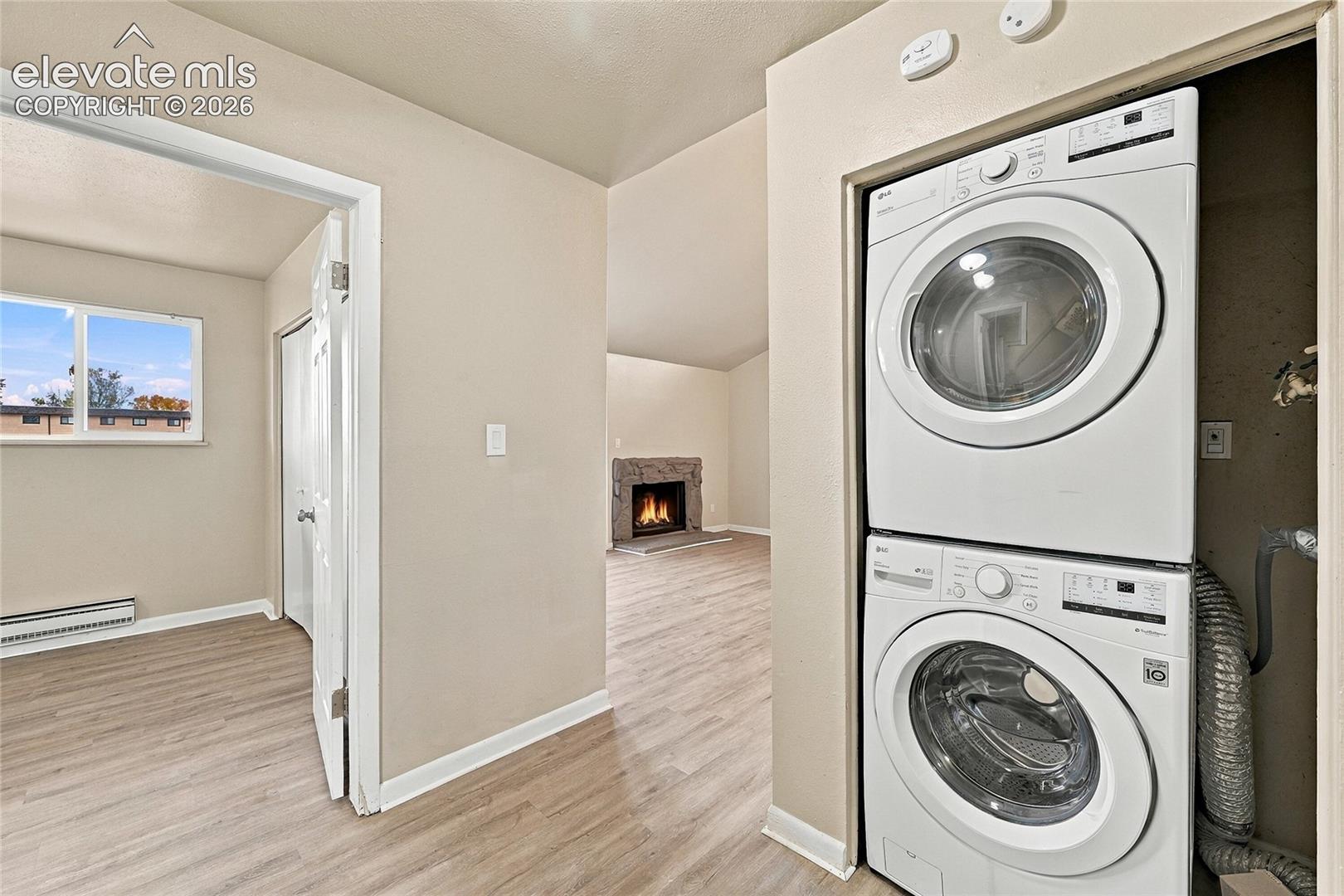 Stacked laundry unit housed in a recessed closet, wood-finish flooring, and a stone-surround fireplace