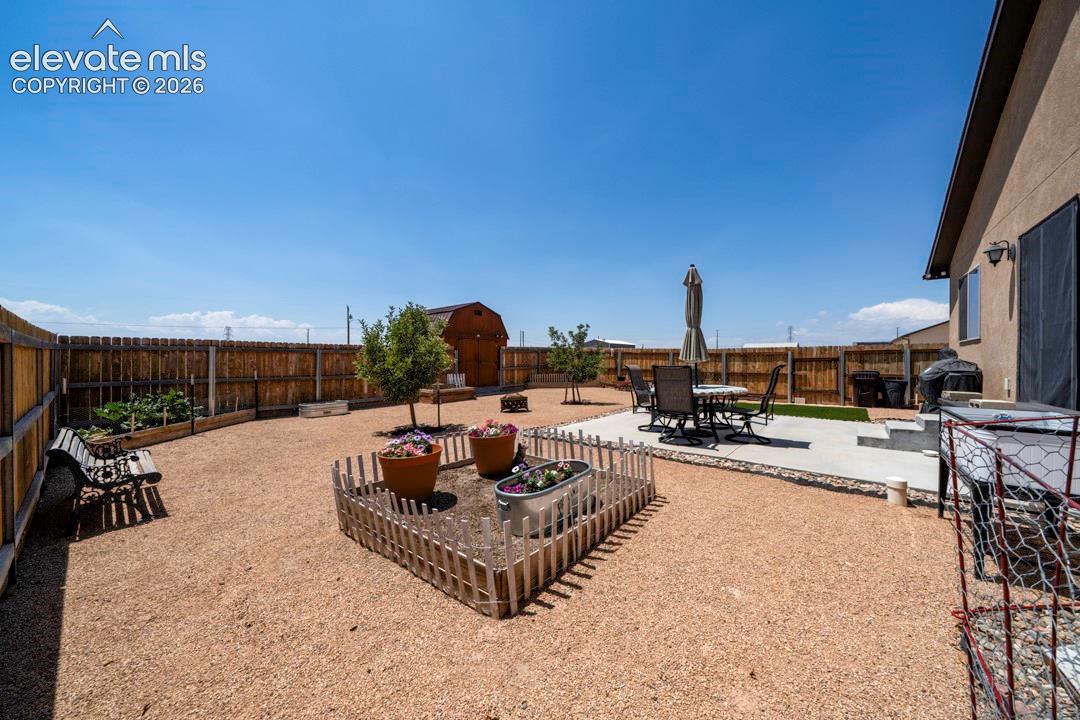 Spacious backyard featuring a privacy fence, gravel landscaping, a concrete patio, a raised garden bed, and a storage shed