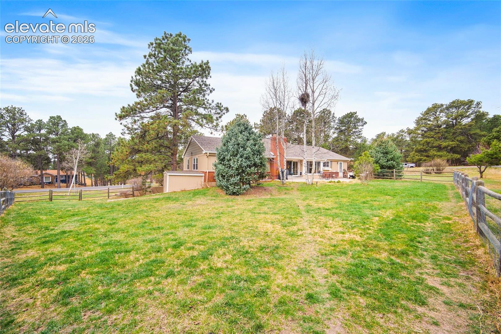 Expansive lot featuring mature pine trees, open grass area, and split-rail perimeter fencing