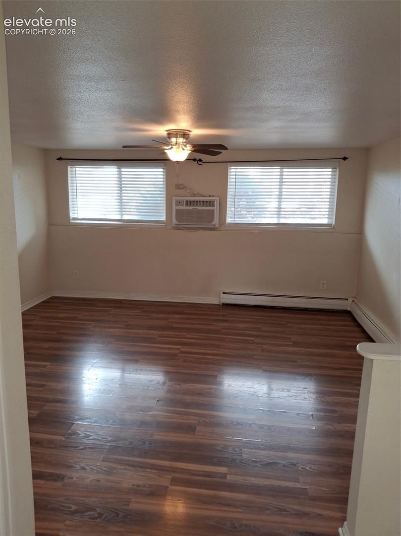 Wood-finish flooring throughout, two windows with horizontal blinds, ceiling fan with integrated lighting, and a wall-mounted air conditioning unit