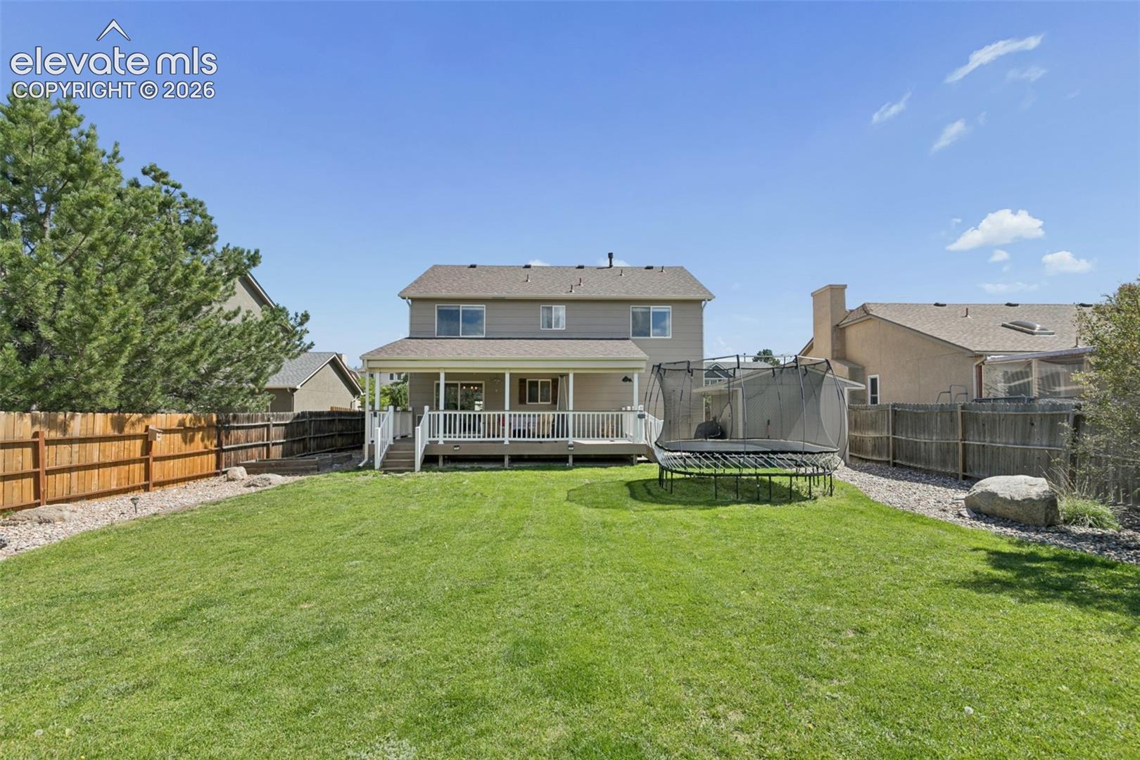 Expansive green lawn with a covered deck, white deck railings, and a wood privacy fence